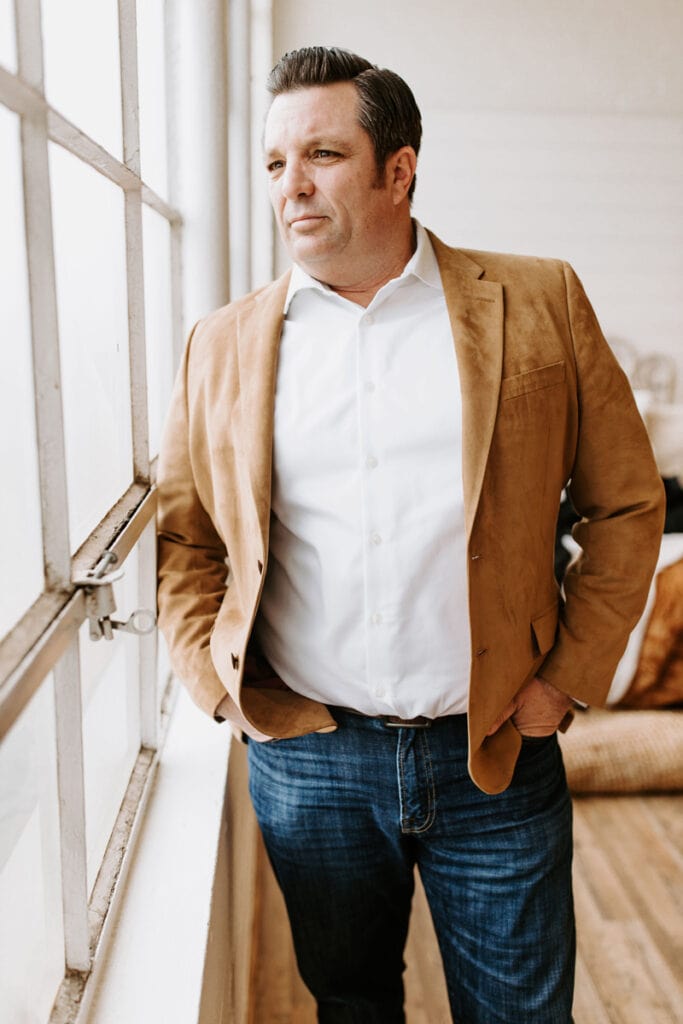 Real Estate Agent Nick Caton posing next to a window with a brown sport coat on